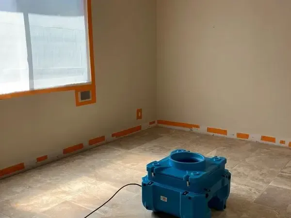 Blue air mover on a bare floor beside a wall marked with orange tape