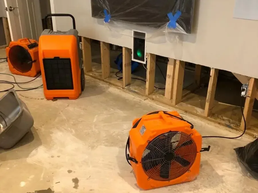 Orange air movers and dehumidifier beside a wall opened along the floor