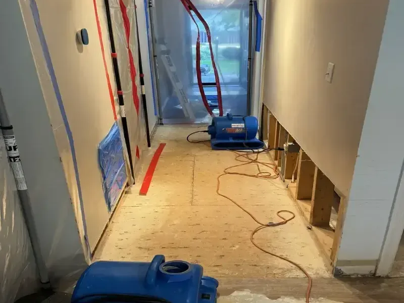 Air movers in a hallway with lower drywall removed and plastic containment