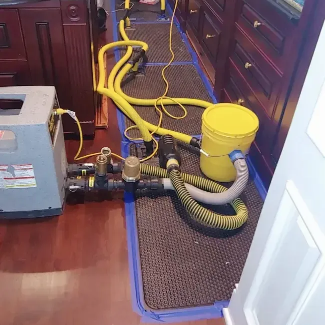 Drying mats connected to hoses cover a wood kitchen floor beside the lower cabinets