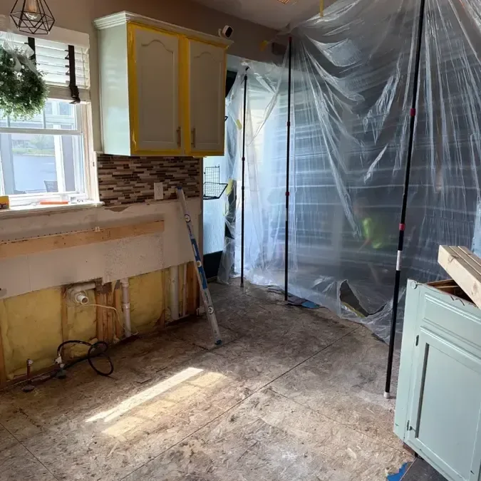 Plastic containment separates a kitchen with its lower cabinets and flooring removed from surrounding space