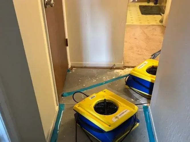 Two yellow air movers in a hallway with baseboards removed