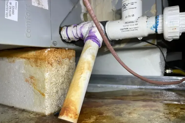Rust staining around the condensate pan and drain connection beneath an air handler