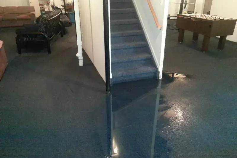 Water covering carpet in a finished lower-level room at the bottom of stairs