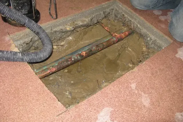 Exposed copper pipe in a concrete-floor trench beside a vacuum hose
