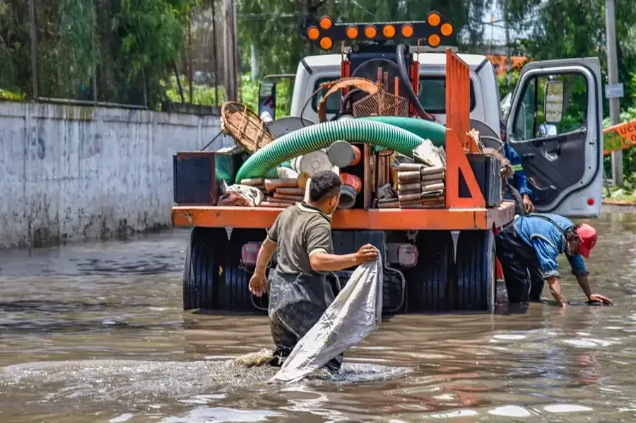 Workers pumping muddy floodwater from a property beside a recovery truck