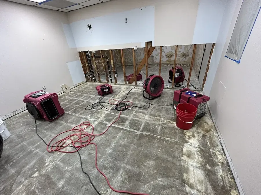 Red air movers and dehumidifiers in a room opened along the wall base