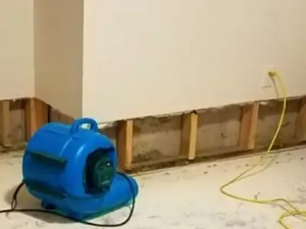 Blue air mover beside exposed framing along the base of a wall