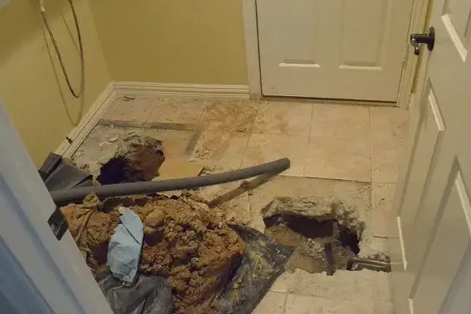 Vacuum hose beside a concrete-floor opening exposing plumbing
